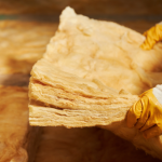 Monteur plaatst een glaswol isolatieplaat met handschoenen in een dakconstructie