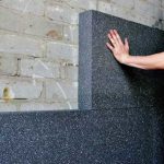 Persoon plaatst een grijze EPS isolatieplaat tegen een muur tijdens gevelisolatie.